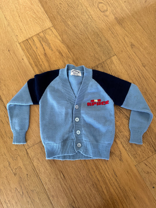 Light blue children's sweater with black and red accents on a wooden floor