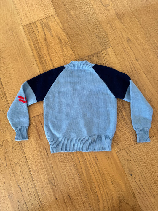 Light blue sweater with dark blue sleeves on a wooden floor